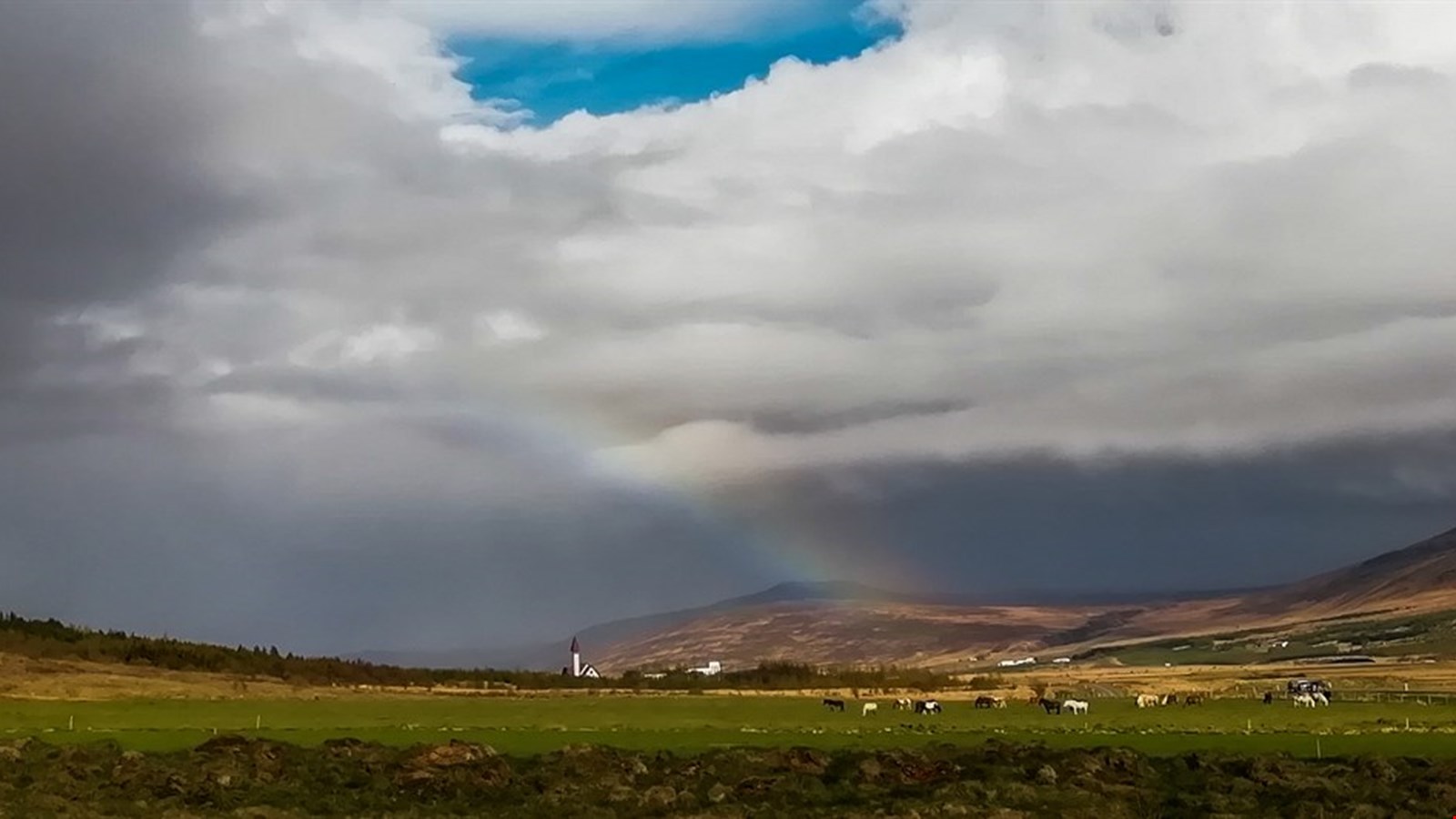 Reykholt landscape with the church tower below clouds and a faint rainbow.