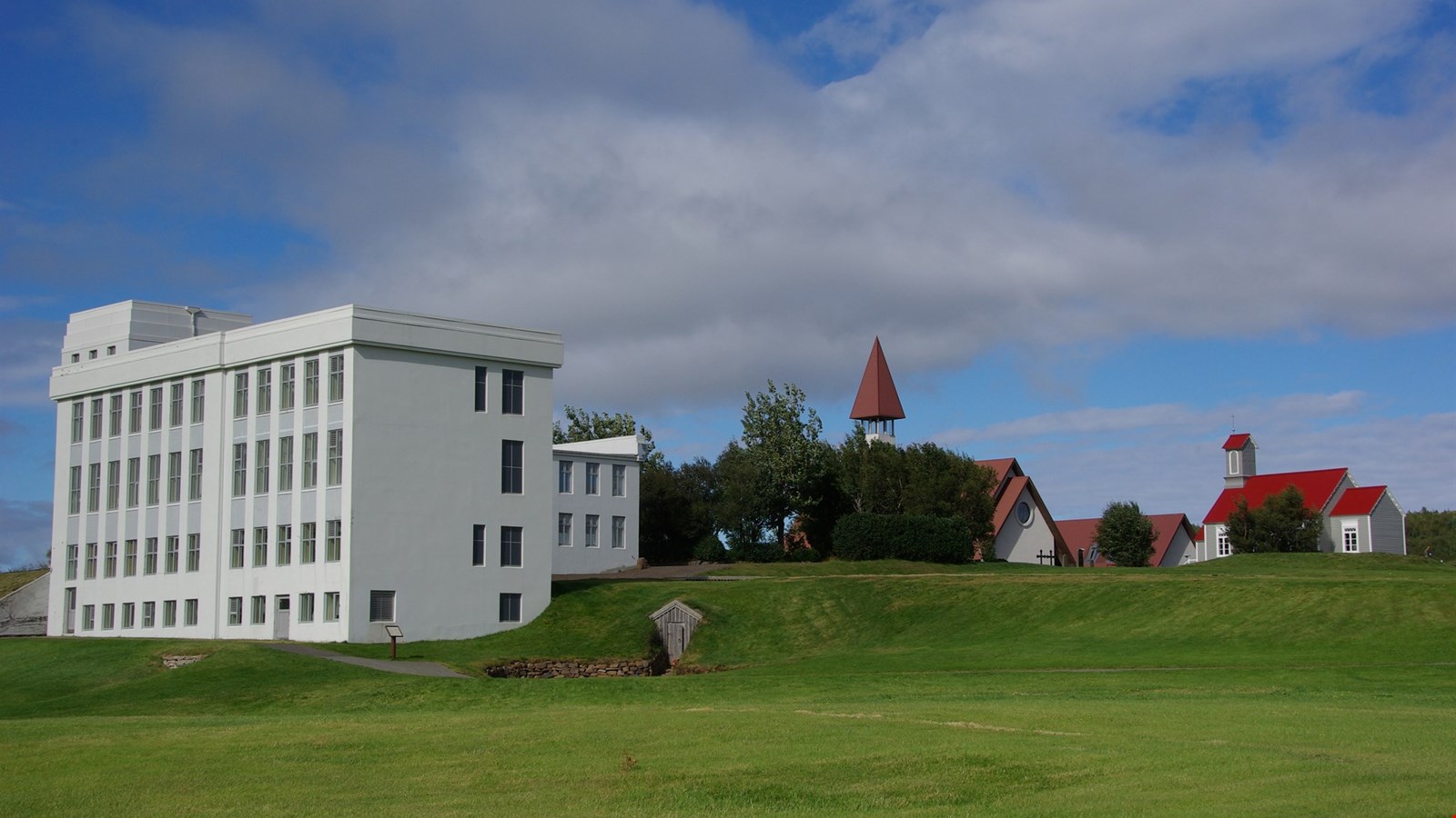 The Snorrastofa visitor buildings and Reykholt church seen across a grassy slope.
