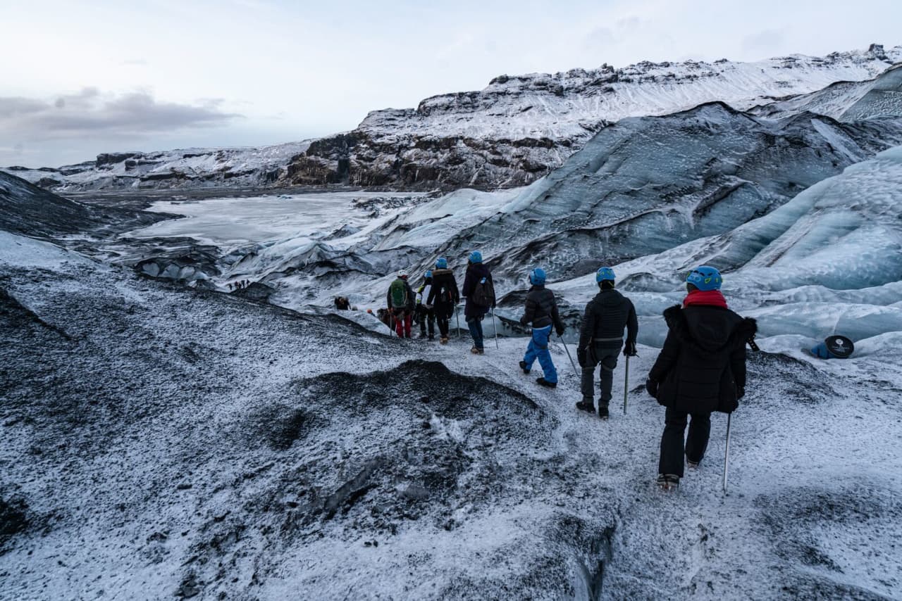 Guided hikers with helmets and poles walking on Sólheimajökull Glacier in winter conditions