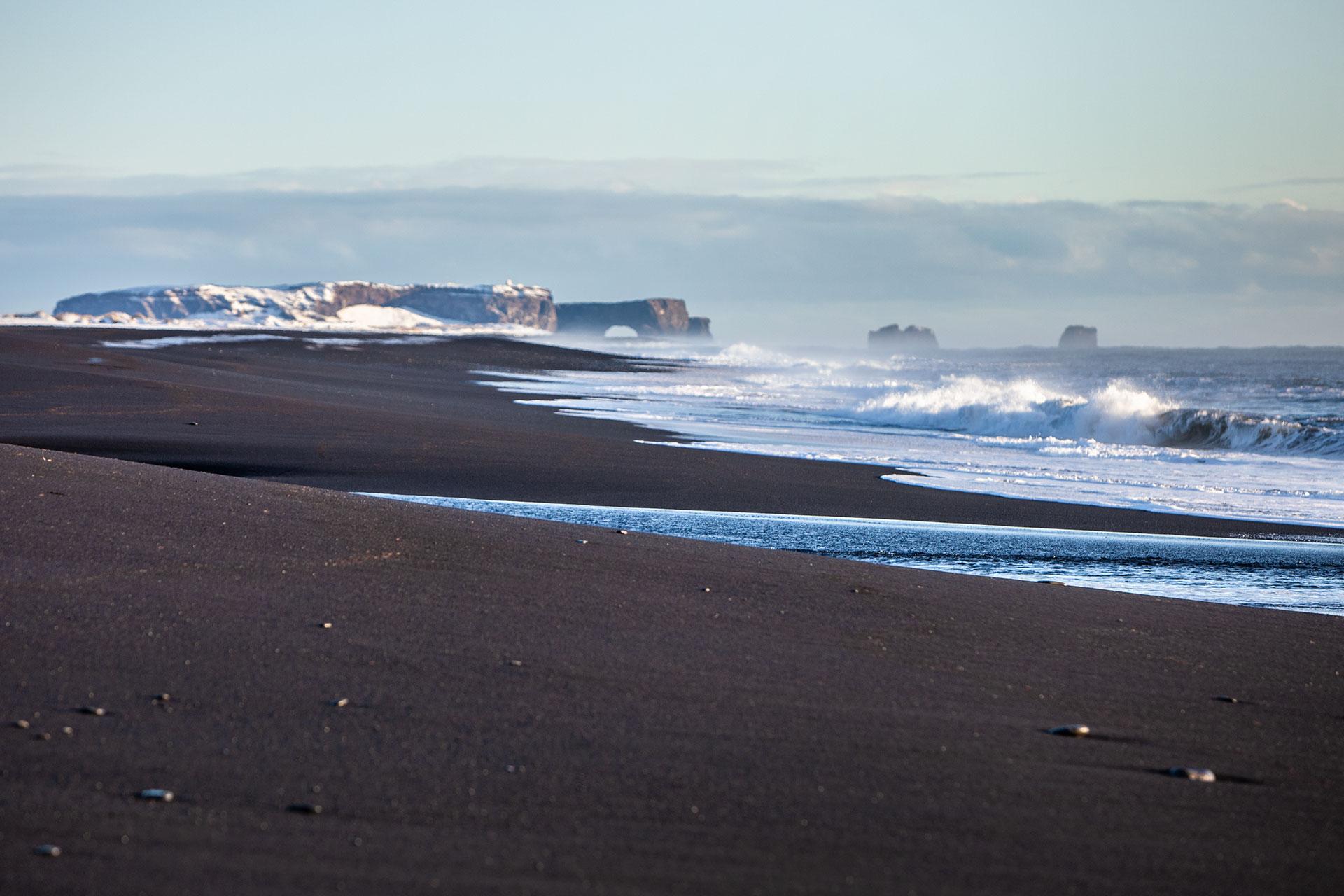 Black sand shoreline near Sólheimasandur with Dyrhólaey and sea stacks in the distance.
