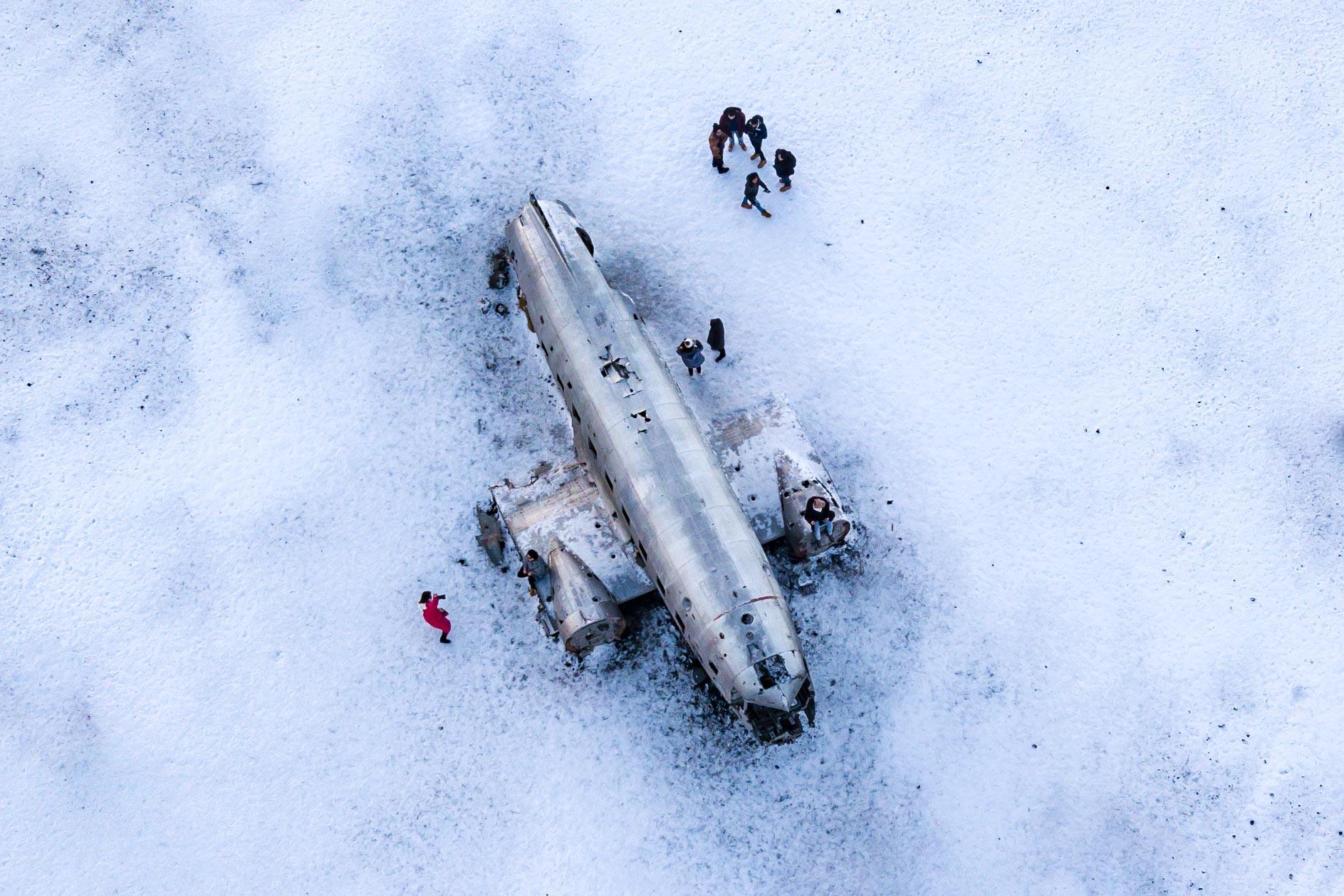 Aerial winter view of the Sólheimasandur DC-3 wreck surrounded by snow and black sand.
