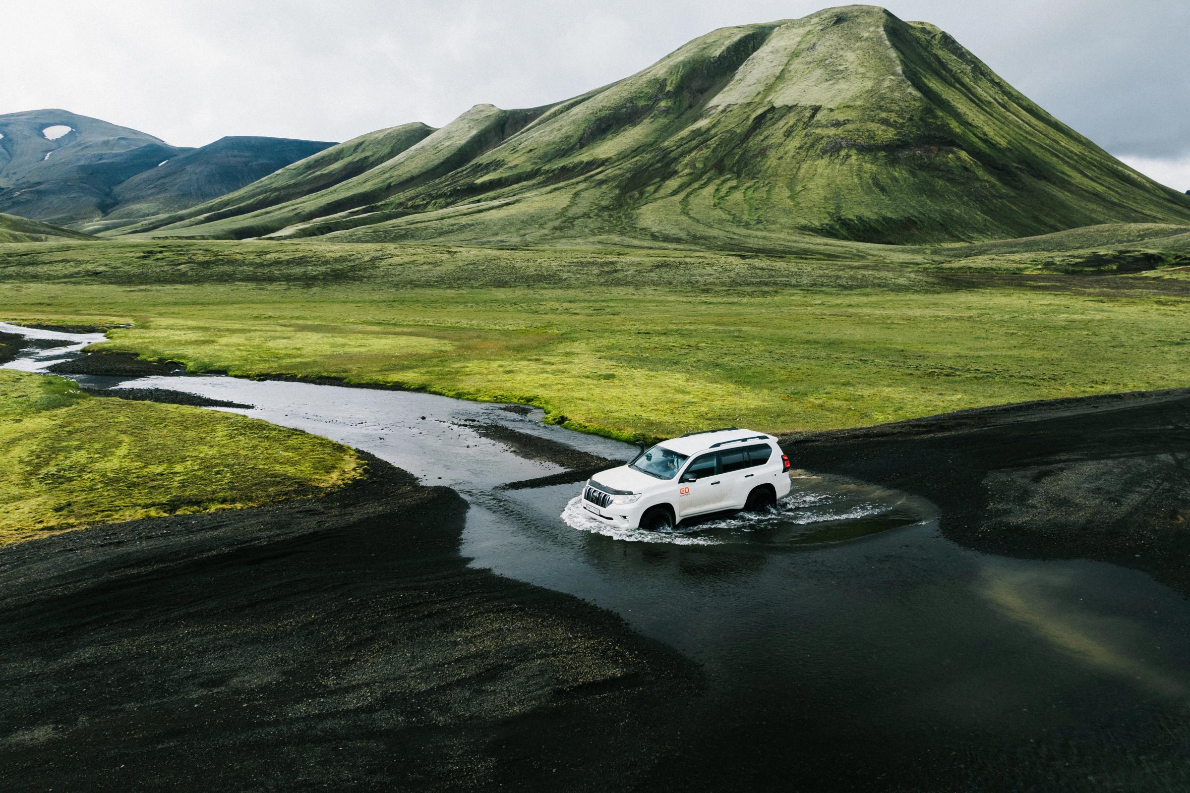 A high-clearance vehicle crossing a shallow river on the rough access route near Stakkholtsgjá.