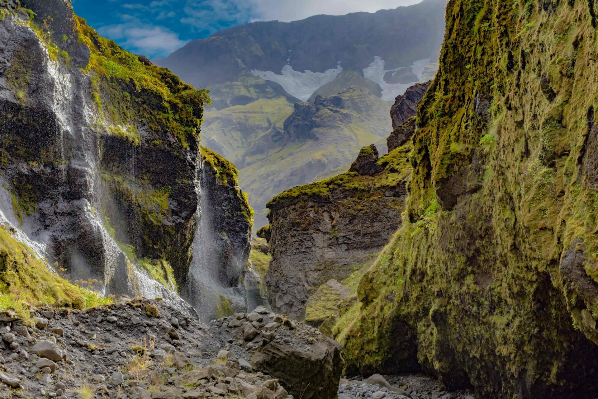 Waterfalls and mossy rock walls inside Stakkholtsgjá with mountains beyond the canyon.