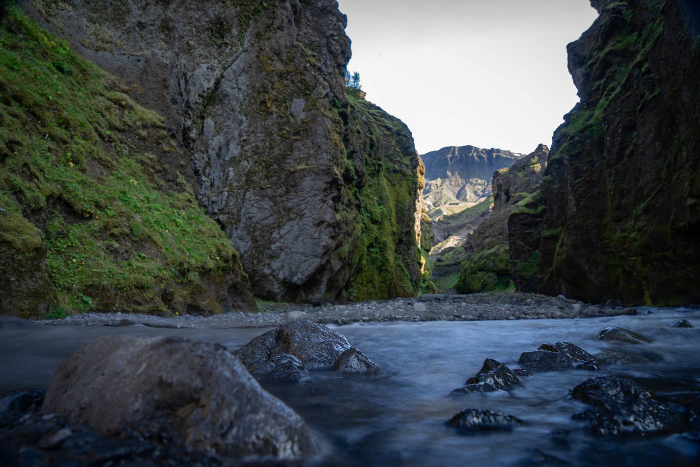 A person standing below tall dark rock walls inside Stakkholtsgjá canyon.