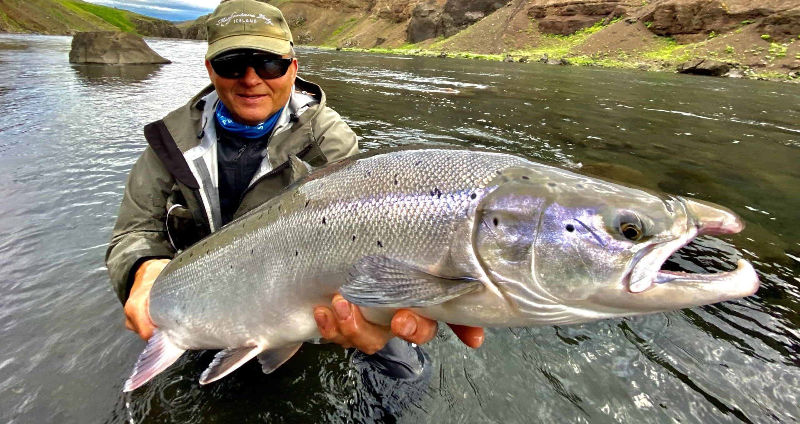 Person fishing in clear Stóra-Laxá water below high canyon walls in South Iceland.
