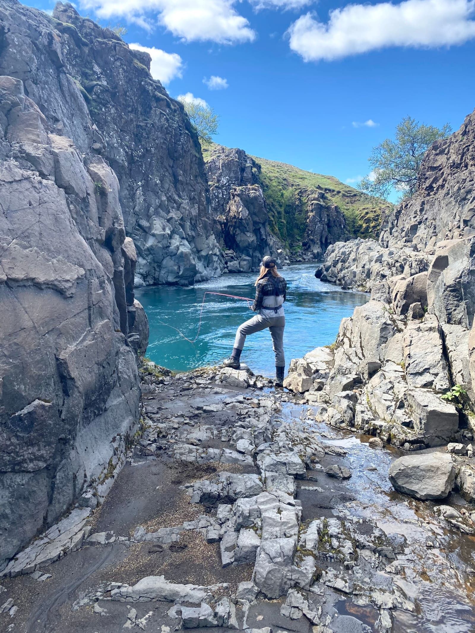 Angler standing beside clear Stóra-Laxá water between steep rock walls in South Iceland.