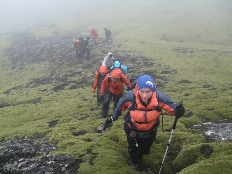 Hikers in rain gear climbing mossy lava slopes near the Bollar craters.