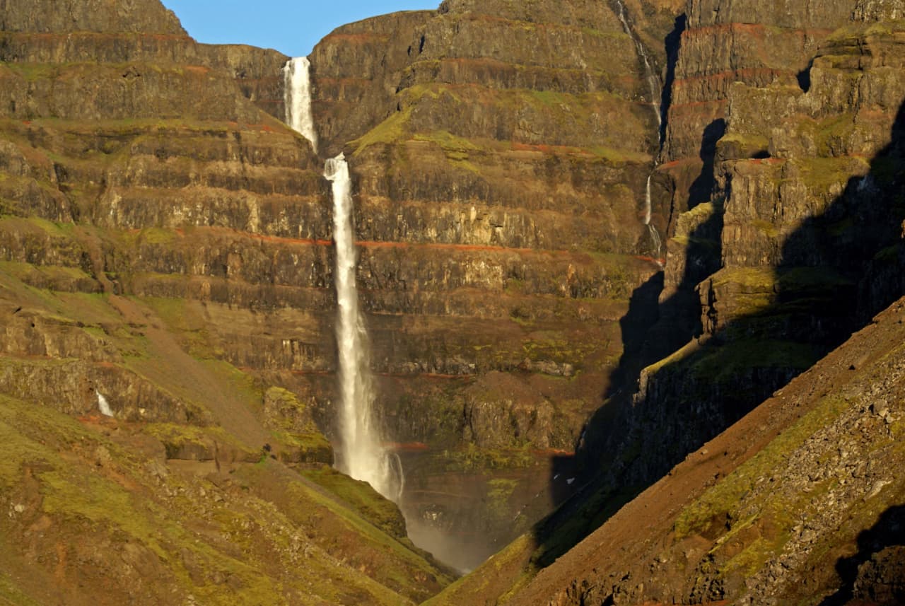 Tighter view of Strútsfoss descending through dark cliffs with visible red bands in East Iceland.