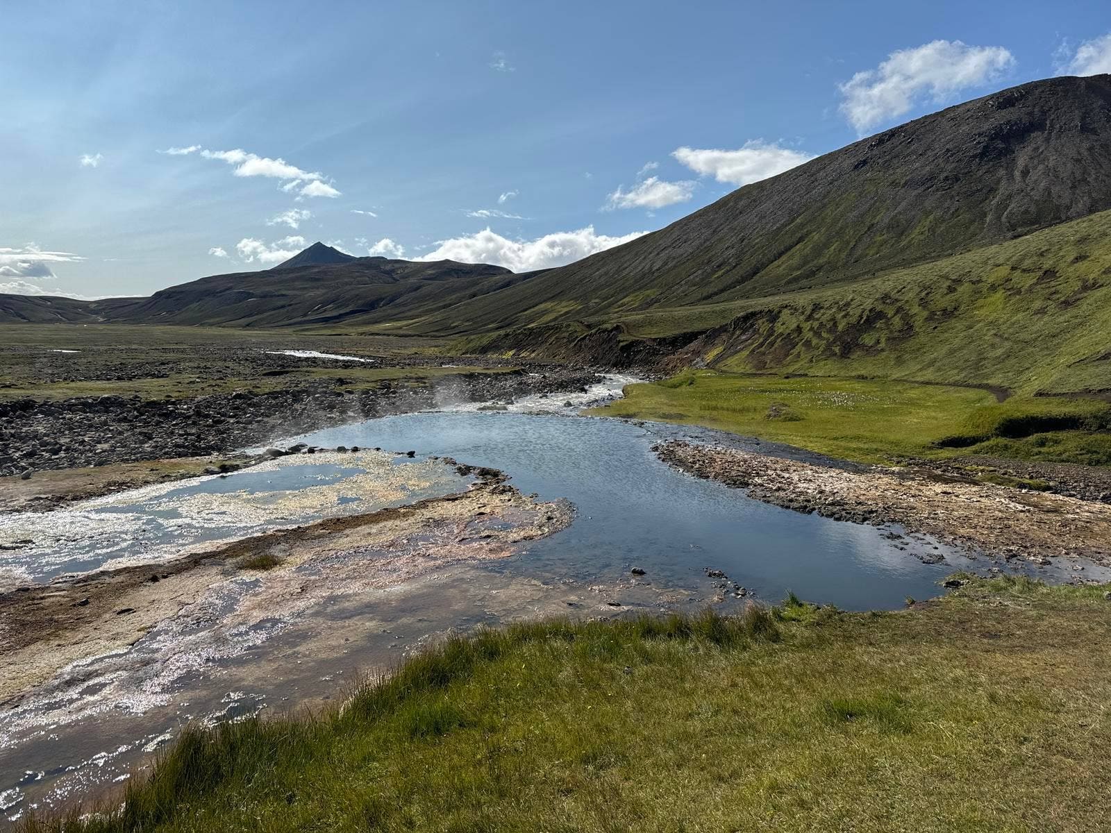 The Strútslaug hot spring pool beside a highland river with dark slopes and a pointed mountain beyond.