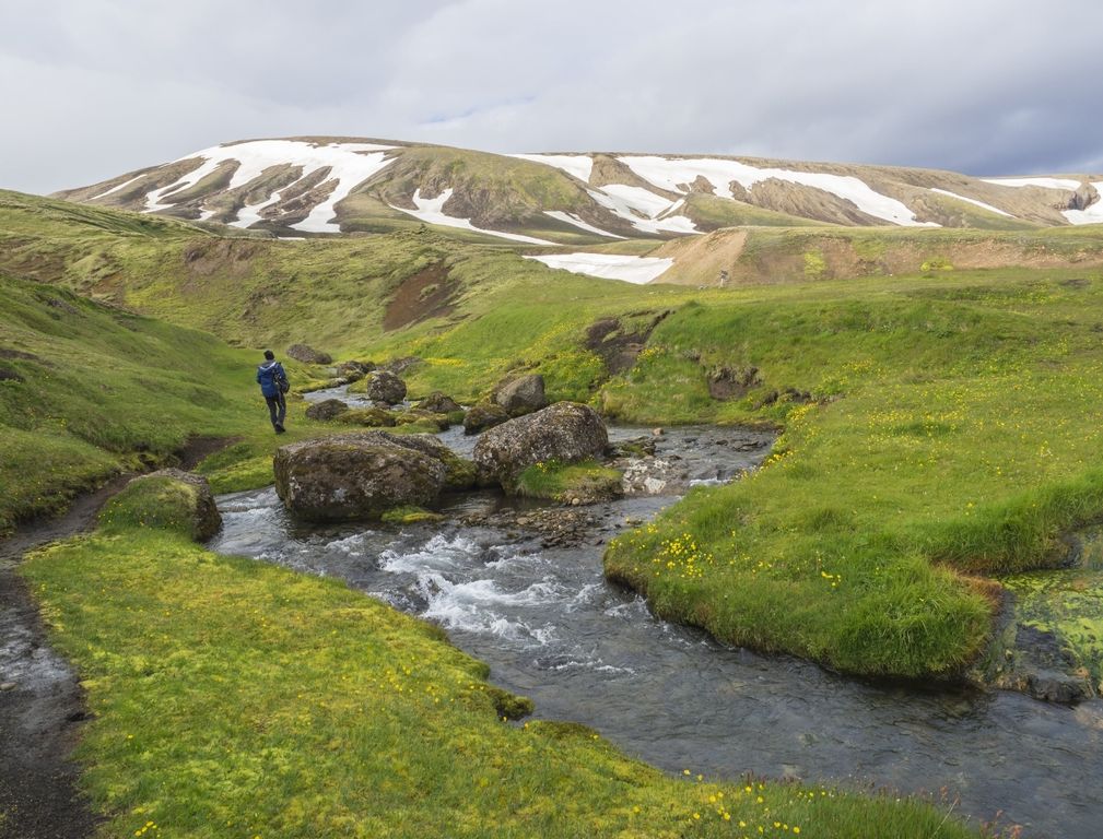 A hiker following a stream through green highland valleys on the approach to Strútslaug.