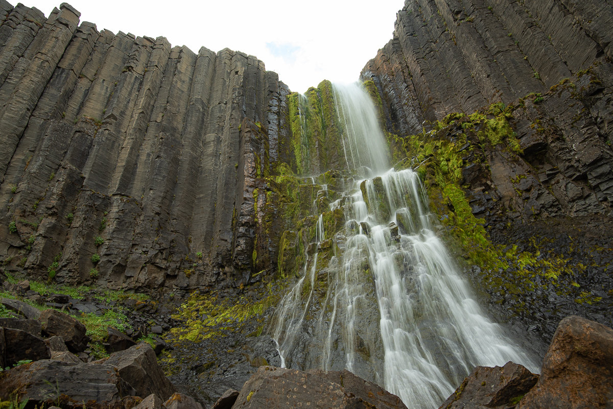 Closer low-angle view of Stuðlafoss with dark basalt columns rising around the waterfall.