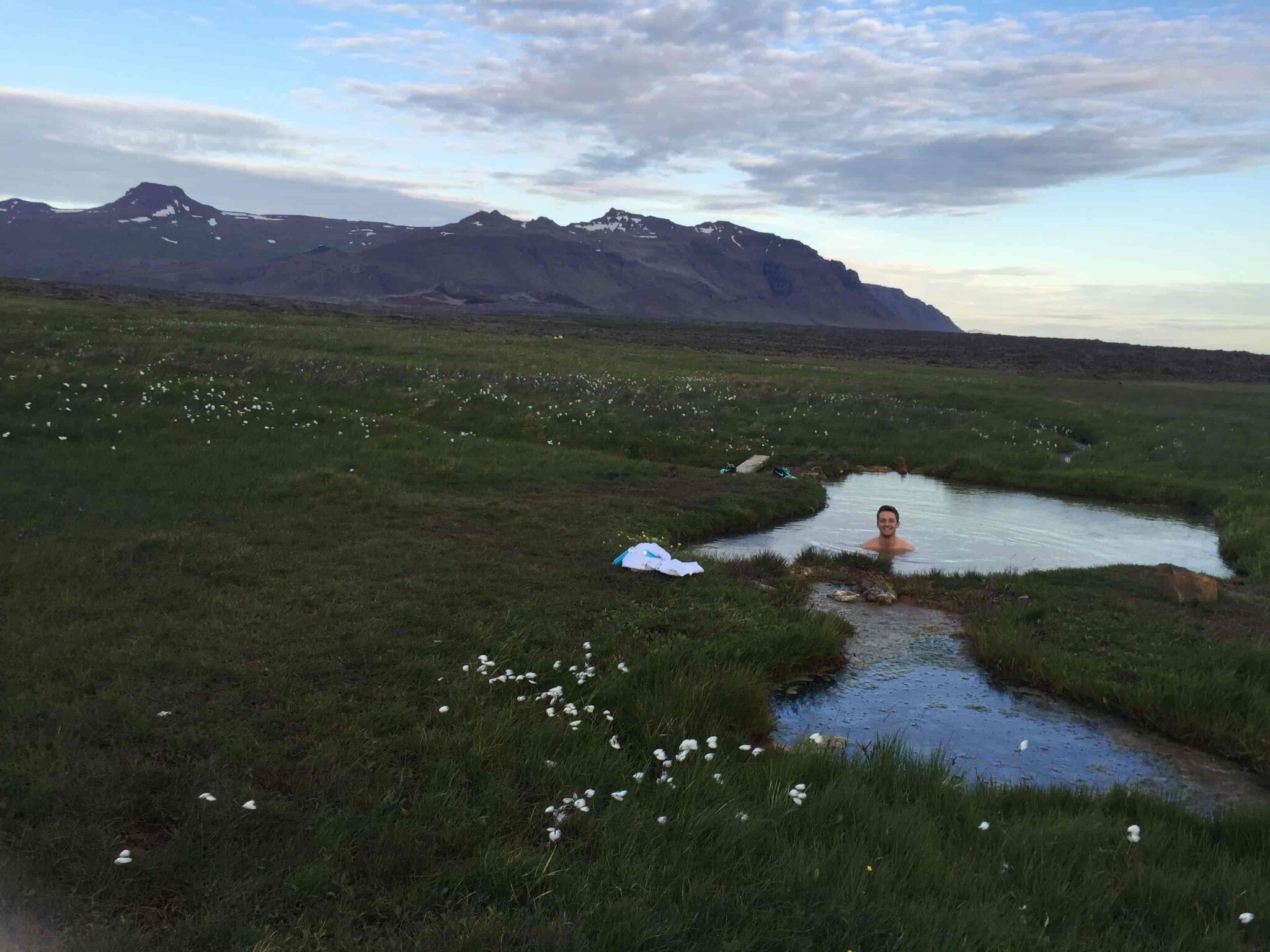 Small geothermal pool at Sturlungalaug Hot Springs with mountains beyond the Snæfellsnes-side grassland.