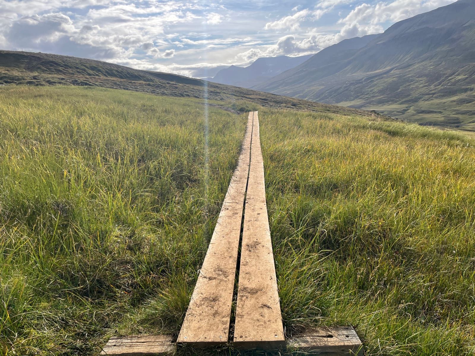 Wooden planks crossing a wet grassy section on the Súlur hiking trail near Akureyri.
