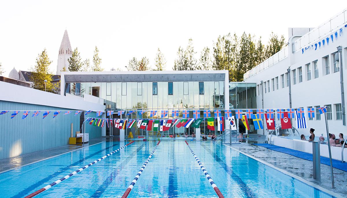 Outdoor lanes at Sundhöllin in central Reykjavík with flags above the pool and a Hallgrímskirkja spire in the background.