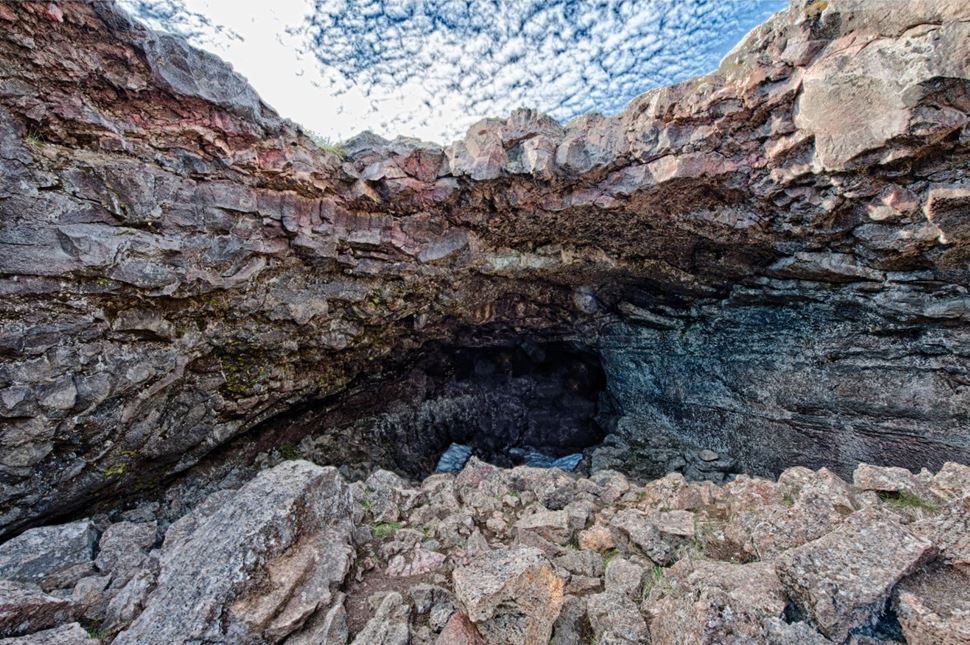 Rocky Surtshellir cave entrance with loose lava blocks and visitors wearing helmets.