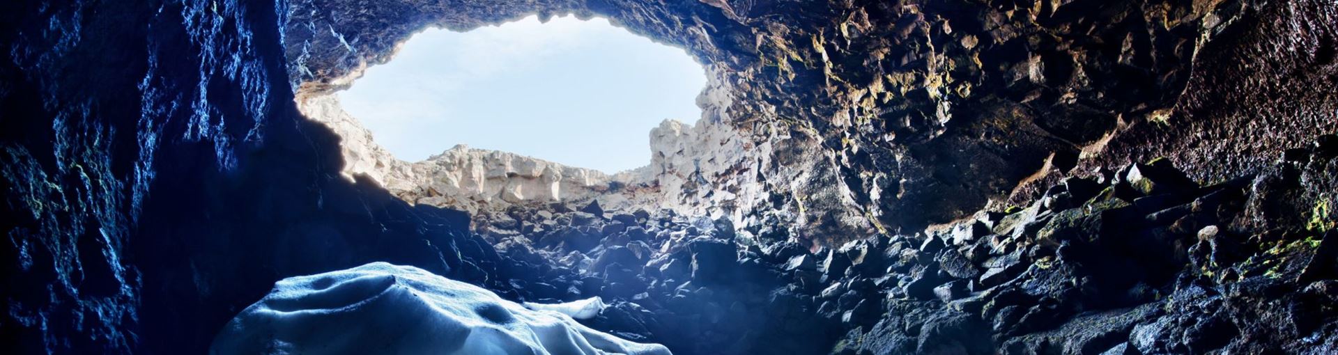 Wide view from inside Surtshellir toward a bright cave opening with ice and rough lava rock.