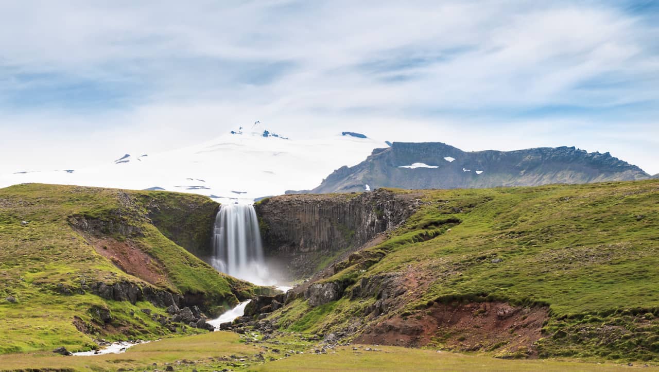 Svöðufoss Waterfall with pale Snæfellsjökull rising behind the basalt rim.
