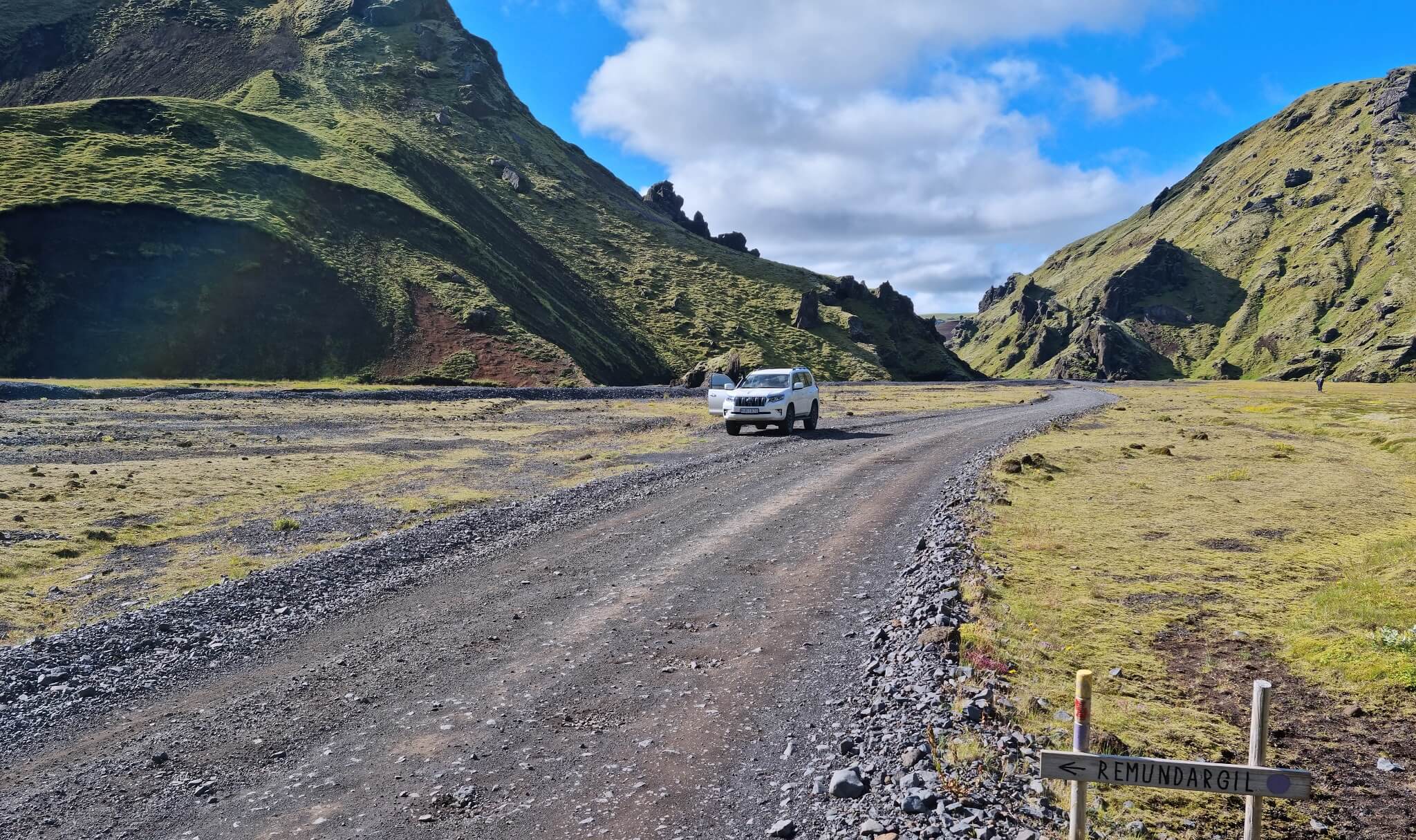 Gravel access road and open basin inside Þakgil, showing the rough approach and hiking trail turnoffs near the canyon floor.