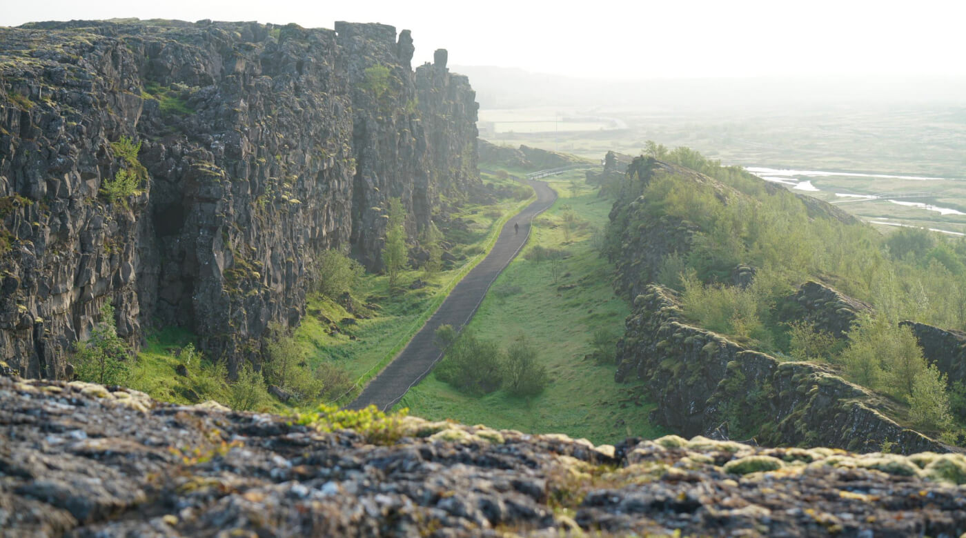 Walking path through Almannagjá at Þingvellir National Park with visitors below the rift cliffs.