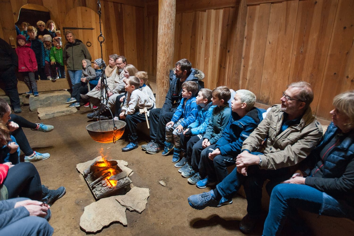 Visitors seated inside the reconstructed Þjóðveldisbærinn longhouse around a hearth.