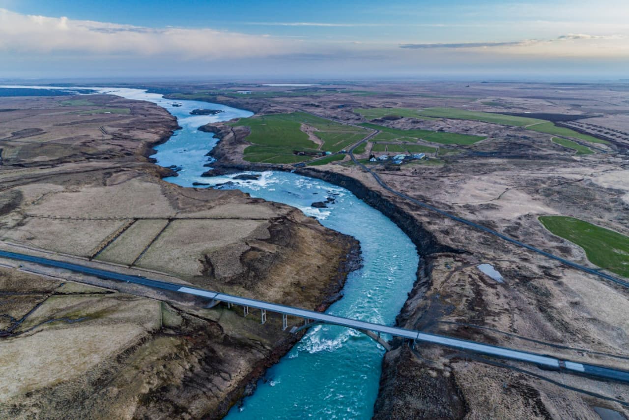 Aerial view of Þjórsá flowing past fields, lava edges, and a road bridge near Urriðafoss in South Iceland.