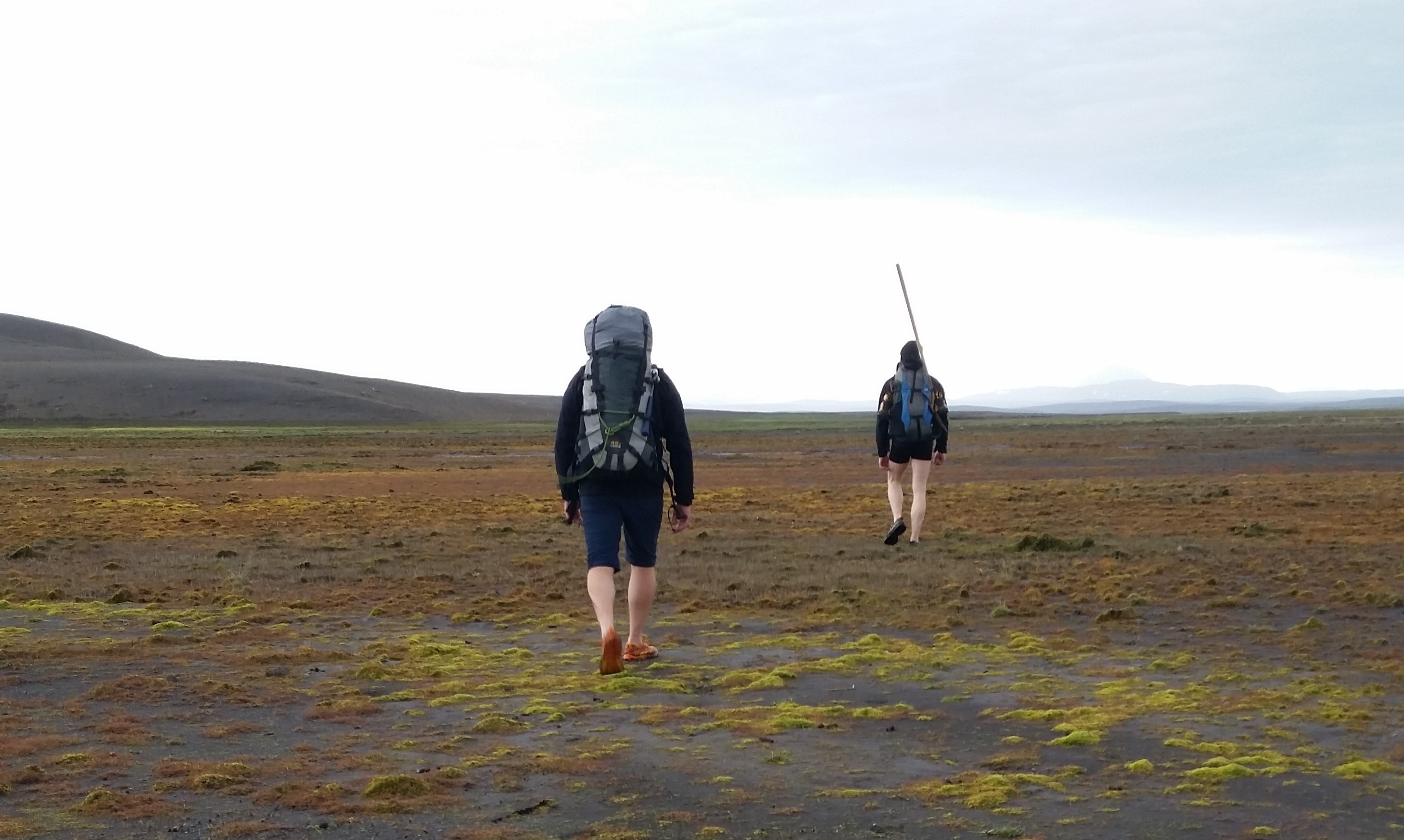 Two hikers crossing mossy highland ground in Þjórsárver with distant mountains ahead.