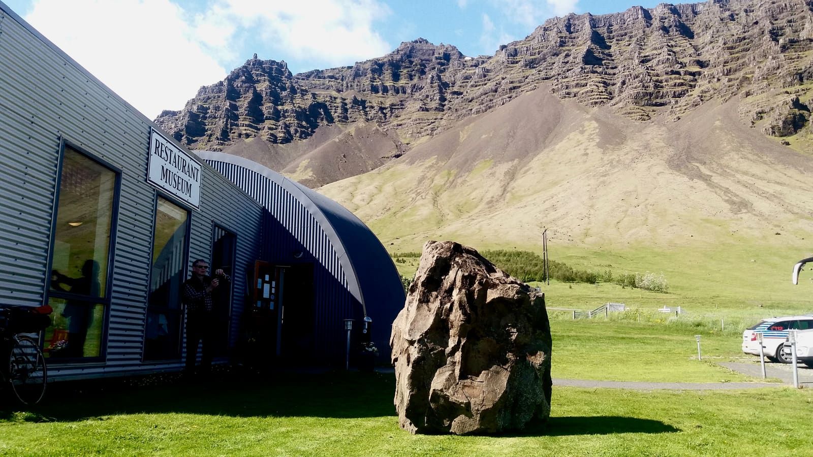 Þórbergssetur entrance at Hali with the museum building, a large stone, and steep Suðursveit mountains behind it.