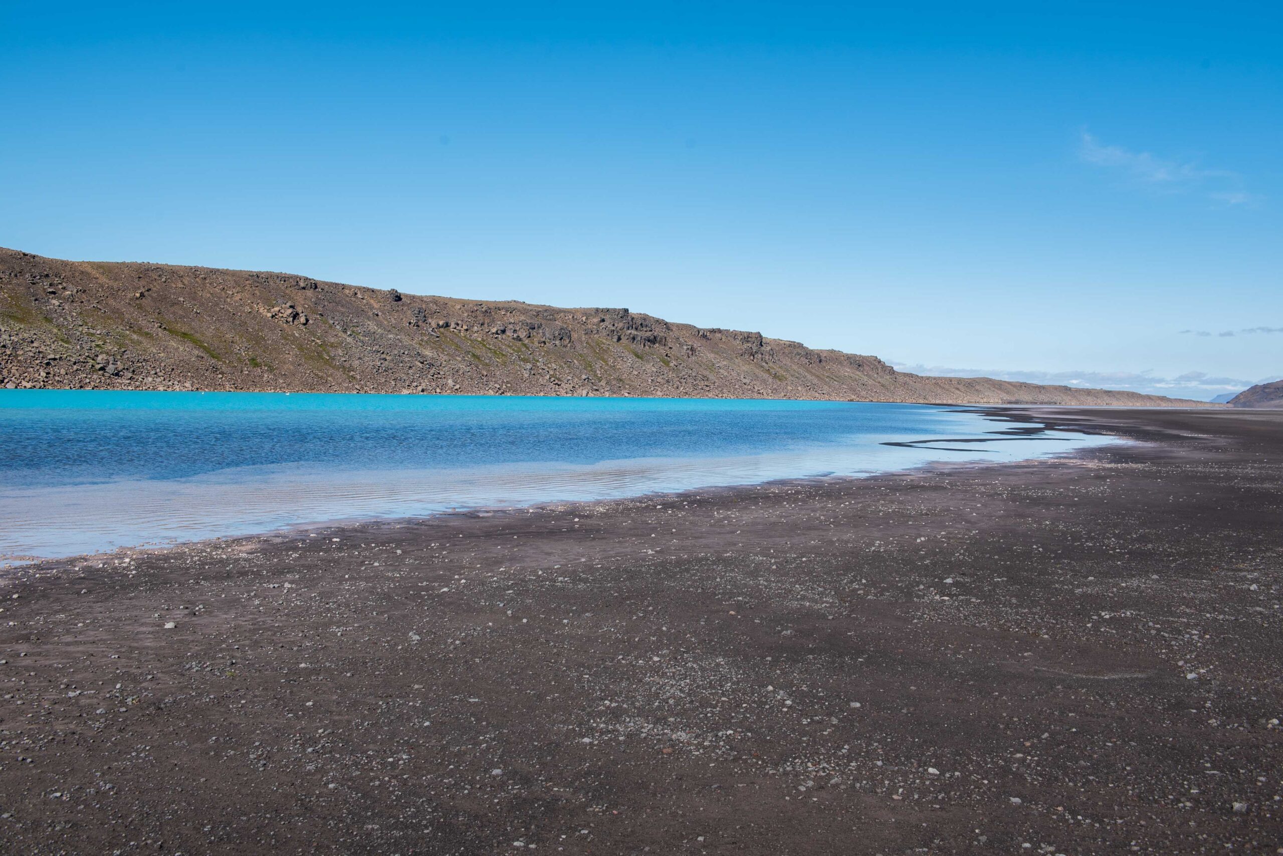 Dark highland slope and bright blue water below the Þórisjökull glacier area.