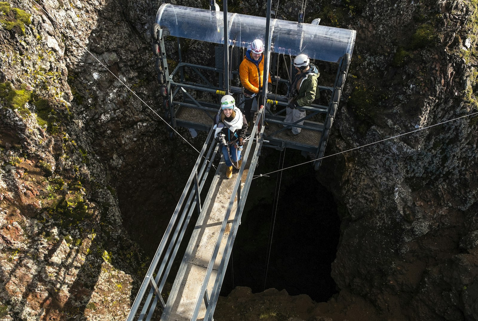 Helmeted visitors standing on the Þríhnúkagígur lift platform above the dark crater opening.