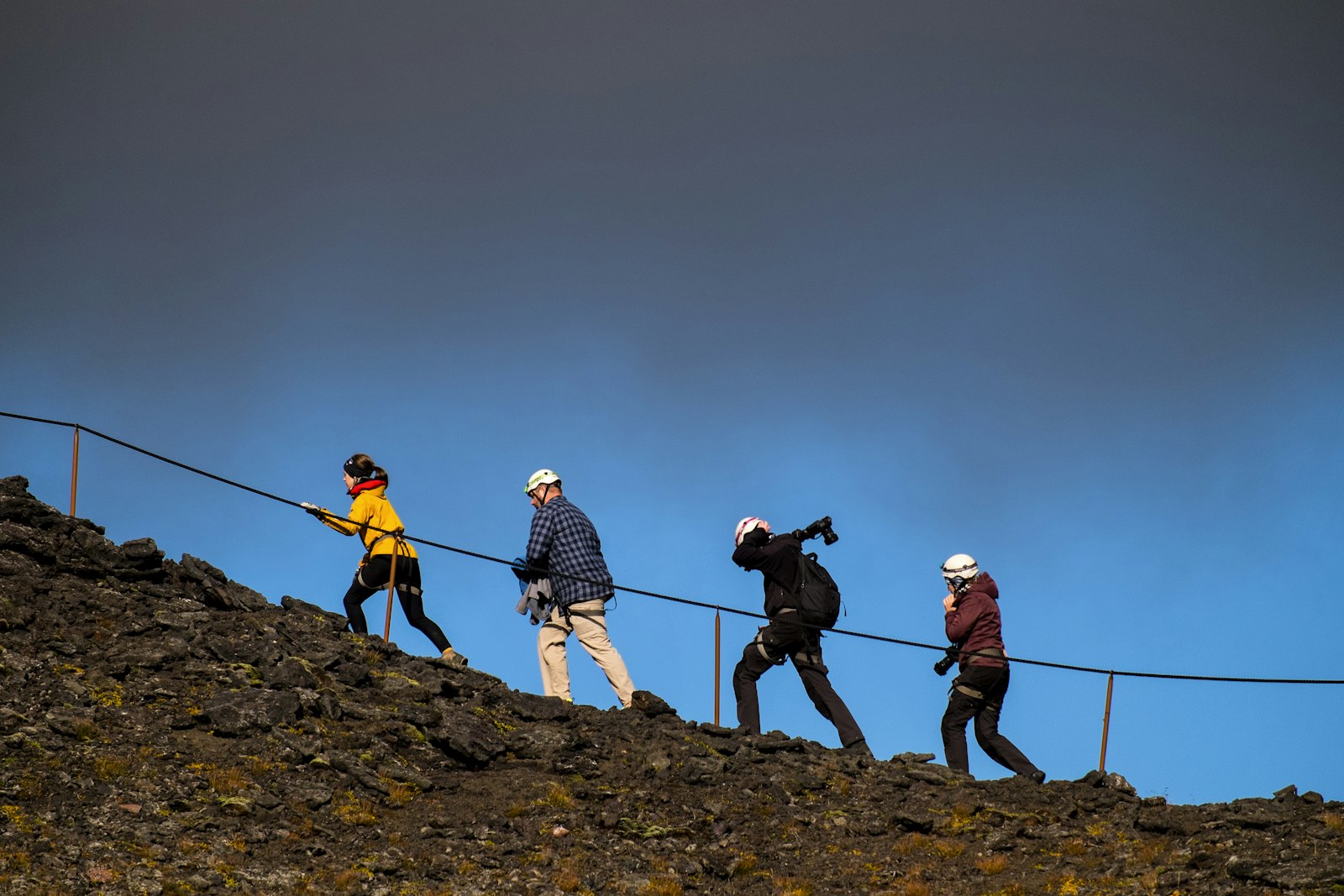 Helmeted visitors following a guide rope over dark lava near the Þríhnúkagígur crater.