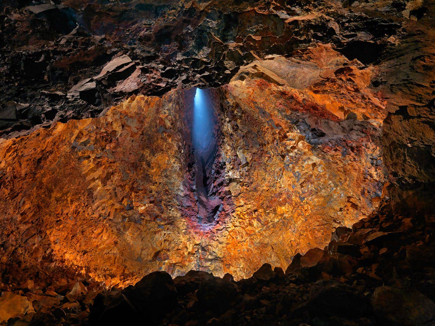 Orange and black mineral-stained rock walls inside the Þríhnúkagígur magma chamber.