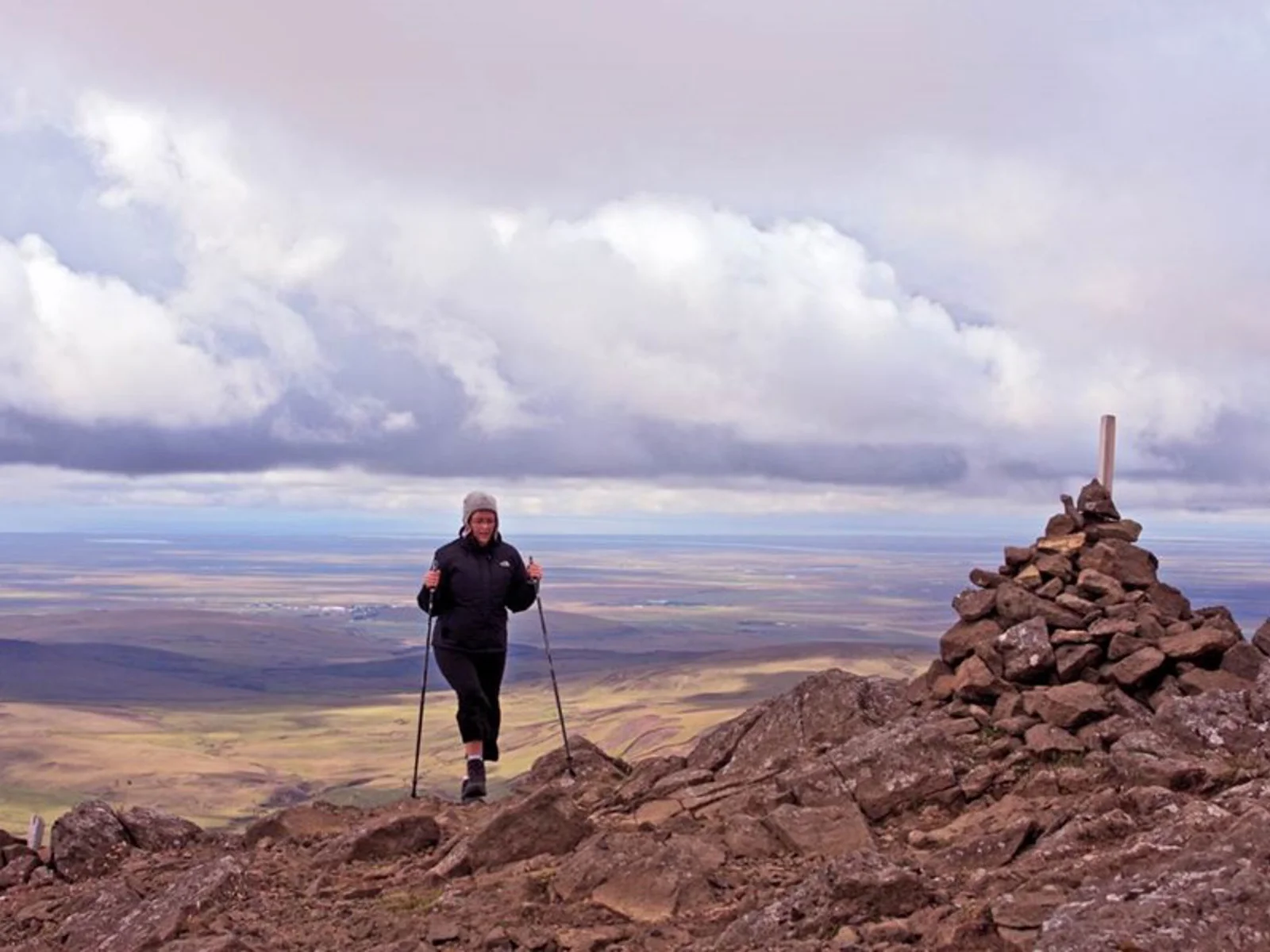 Hiker beside a stone cairn on Þríhyrningur summit with South Iceland lowlands below.