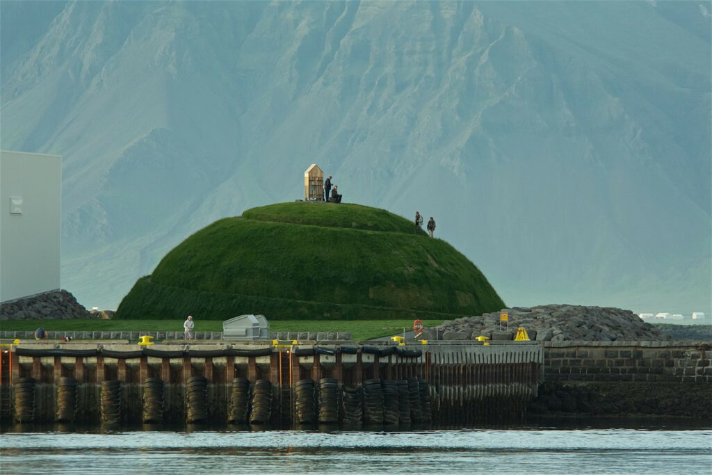Þúfa's green mound rising above Reykjavík harbour with mountains behind it
