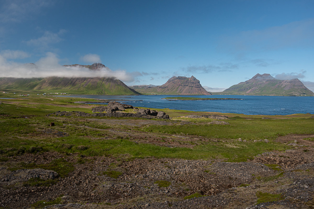 Wide view across Trékyllisvík and Norðurfjörður with green shoreline, blue water, and steep Strandir mountains.