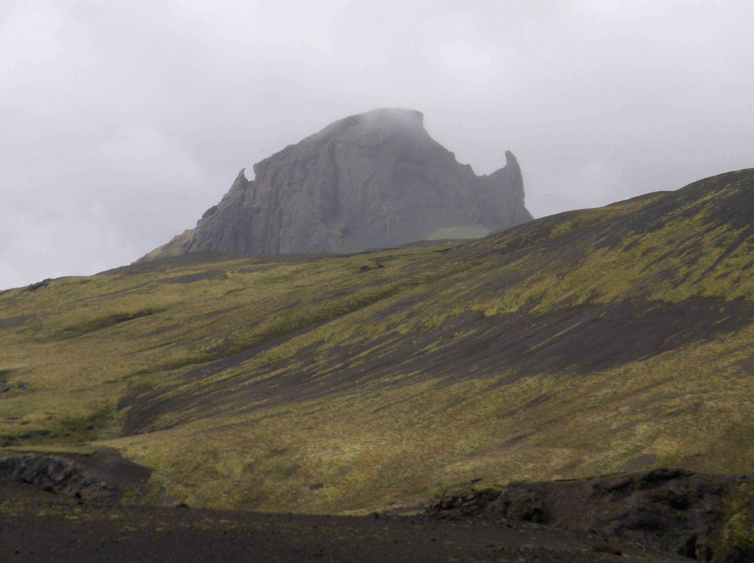 Einhyrningur rising through low cloud above green and black highland slopes in South Iceland.