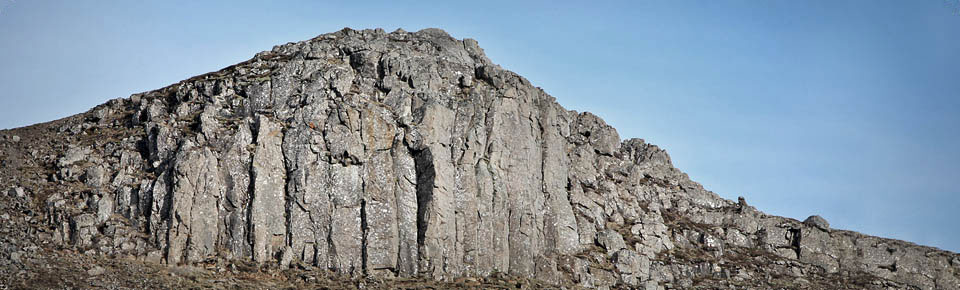 Wide view of the gray basalt face at Valshamar above grassy ground.