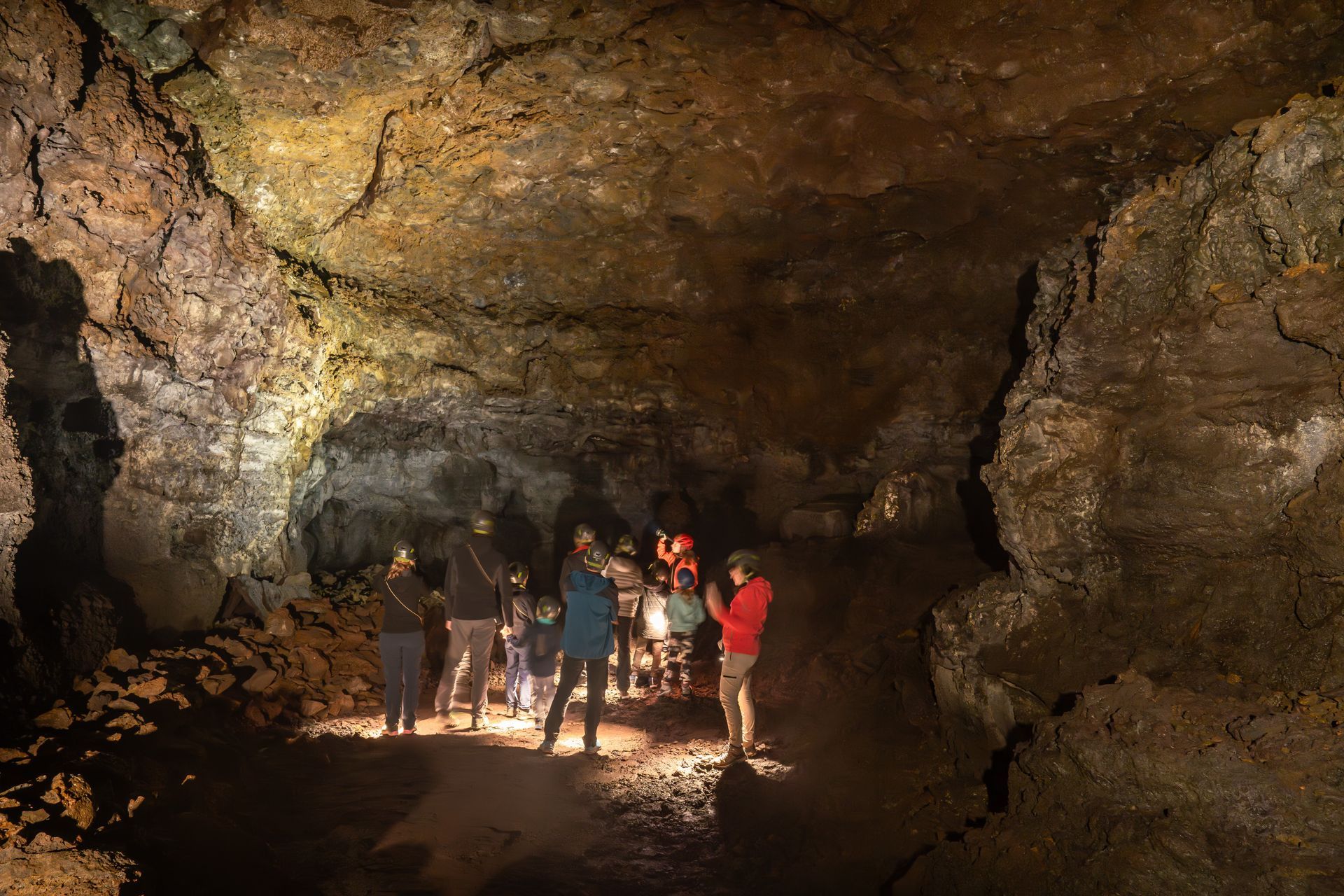 Guided visitors with helmets and lights standing on uneven lava ground inside Vatnshellir Cave.