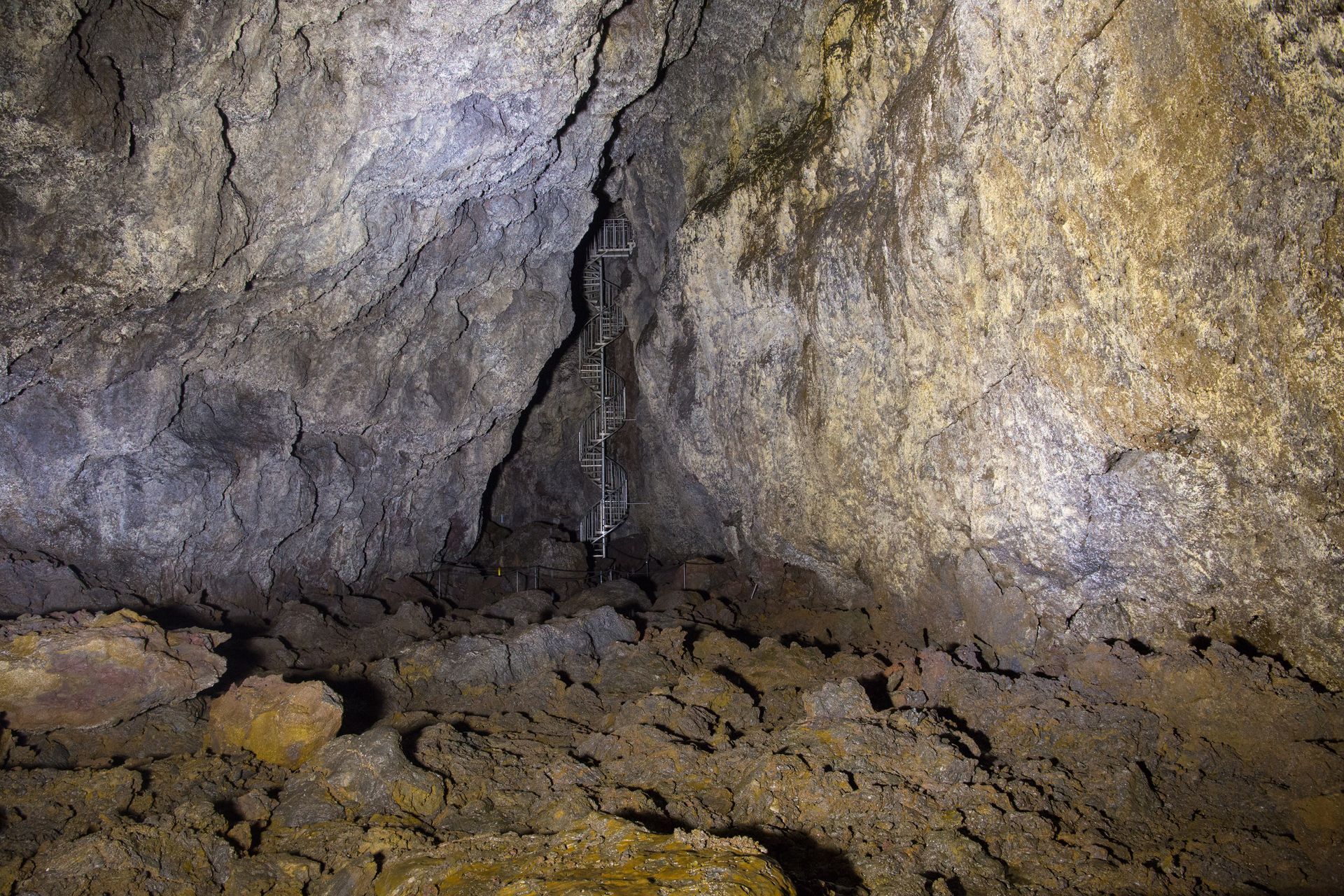 Metal staircase descending through the rough lava walls inside Vatnshellir Cave.