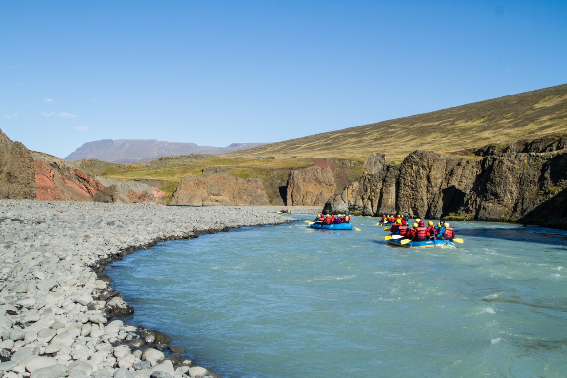 Rafts floating through the pale Vestari Jökulsá river below rocky canyon walls in Skagafjörður.
