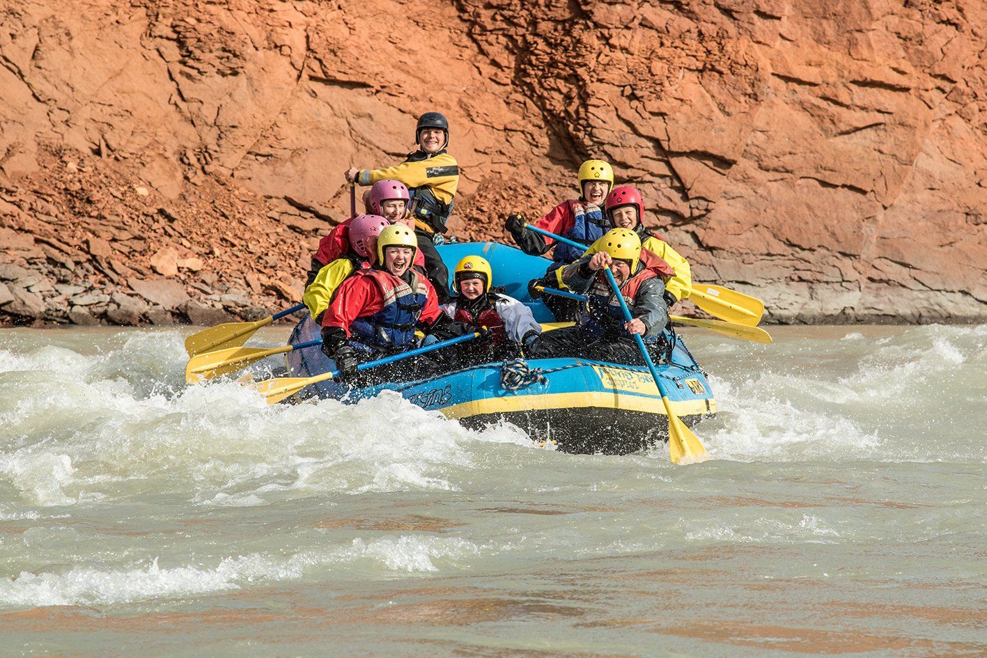 A helmeted rafting group paddling through low rapids below red canyon rock on Vestari Jökulsá.