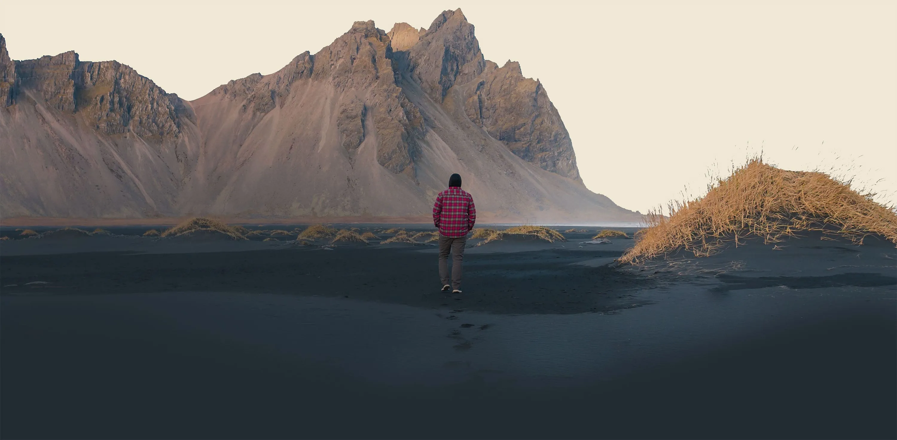 Traveler standing on black sand beneath the sharp wall of Vestrahorn at Stokksnes.