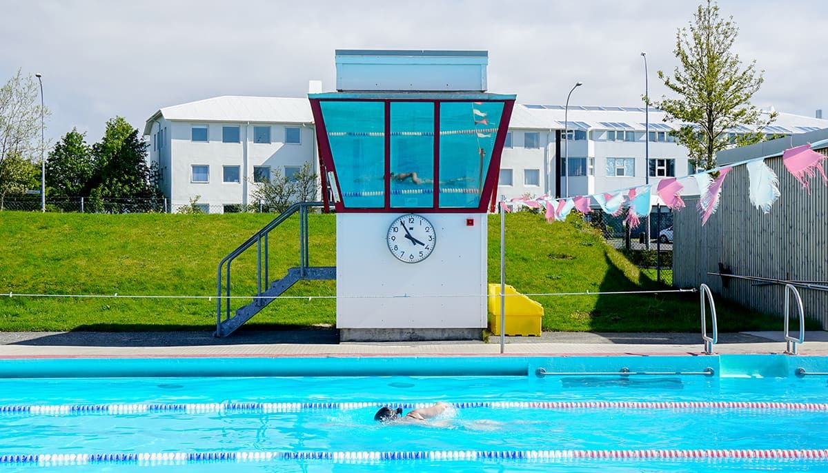 Swimmer in the outdoor pool at Vesturbæjarlaug with the red-framed watchtower behind the lap lanes.