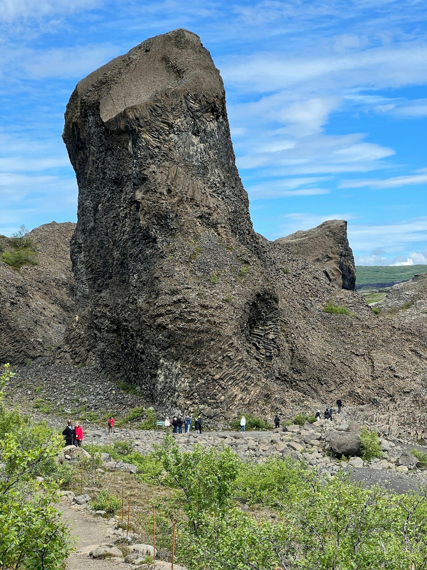 Visitors walking below the Tröllið basalt formation in Vesturdalur Valley.