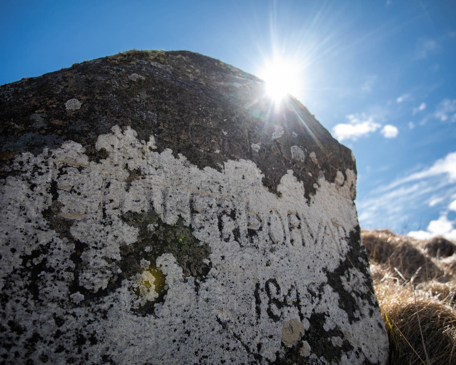 Weathered inscribed stone on Viðey with lichen and carved letters