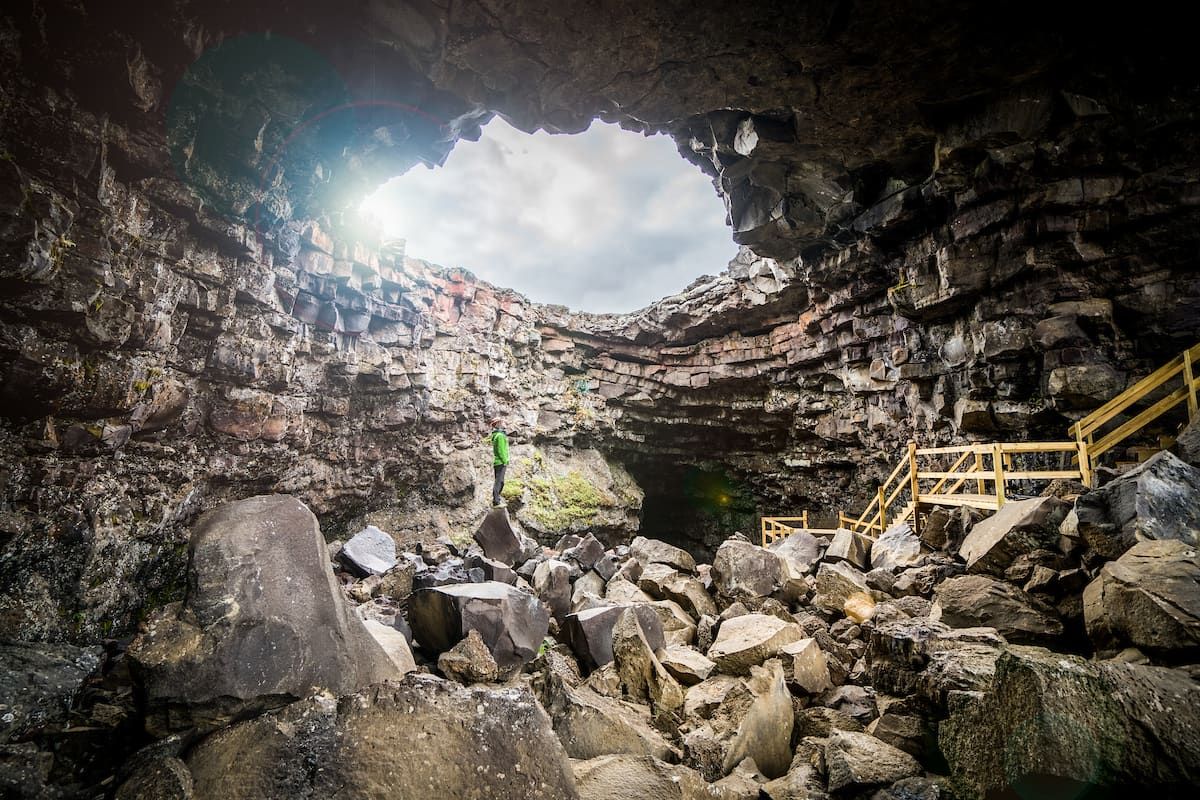 Wooden steps and a guide at the rocky entrance of Víðgelmir lava cave in West Iceland.