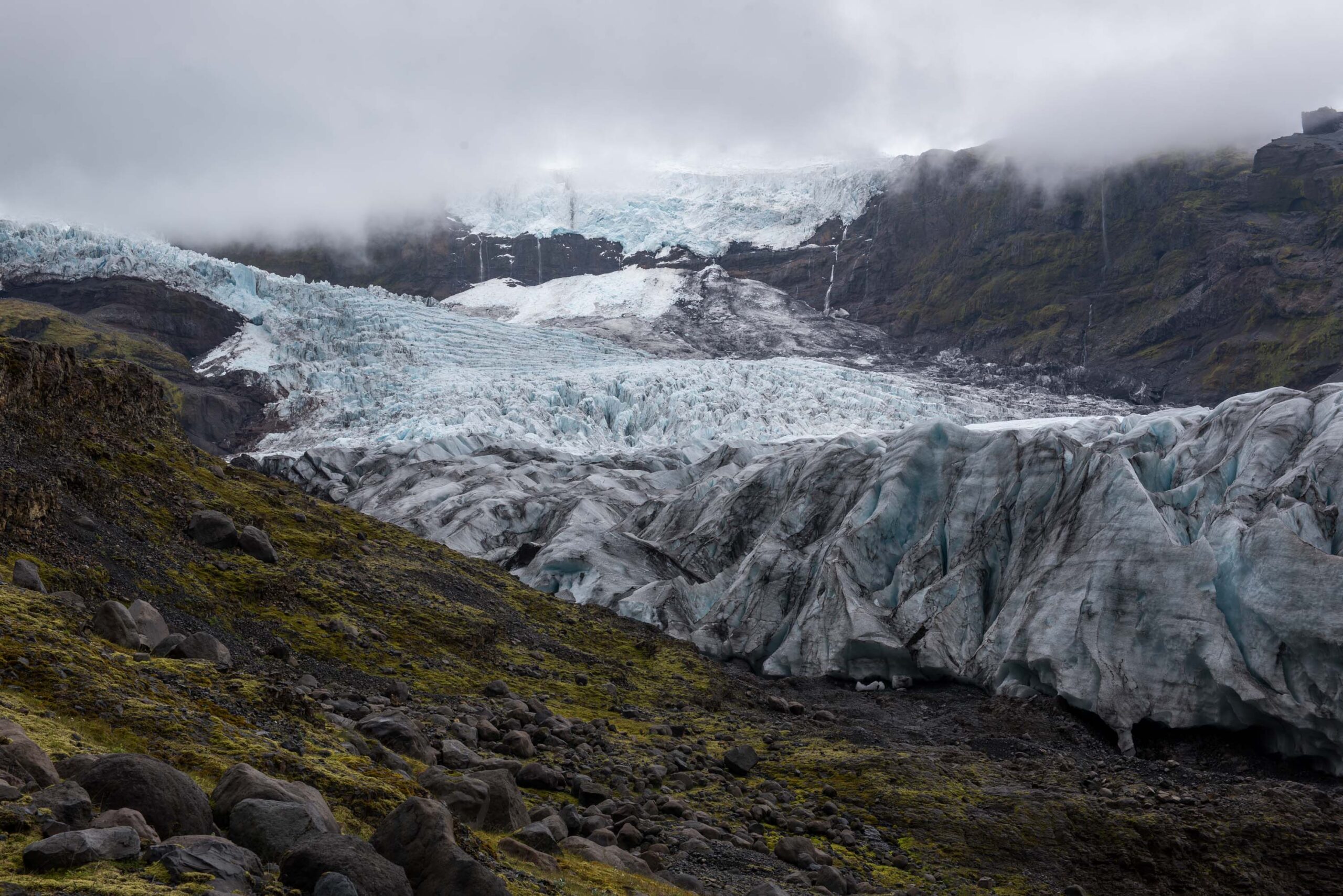Blue and debris-covered ice on Virkisjökull below dark mountain slopes.