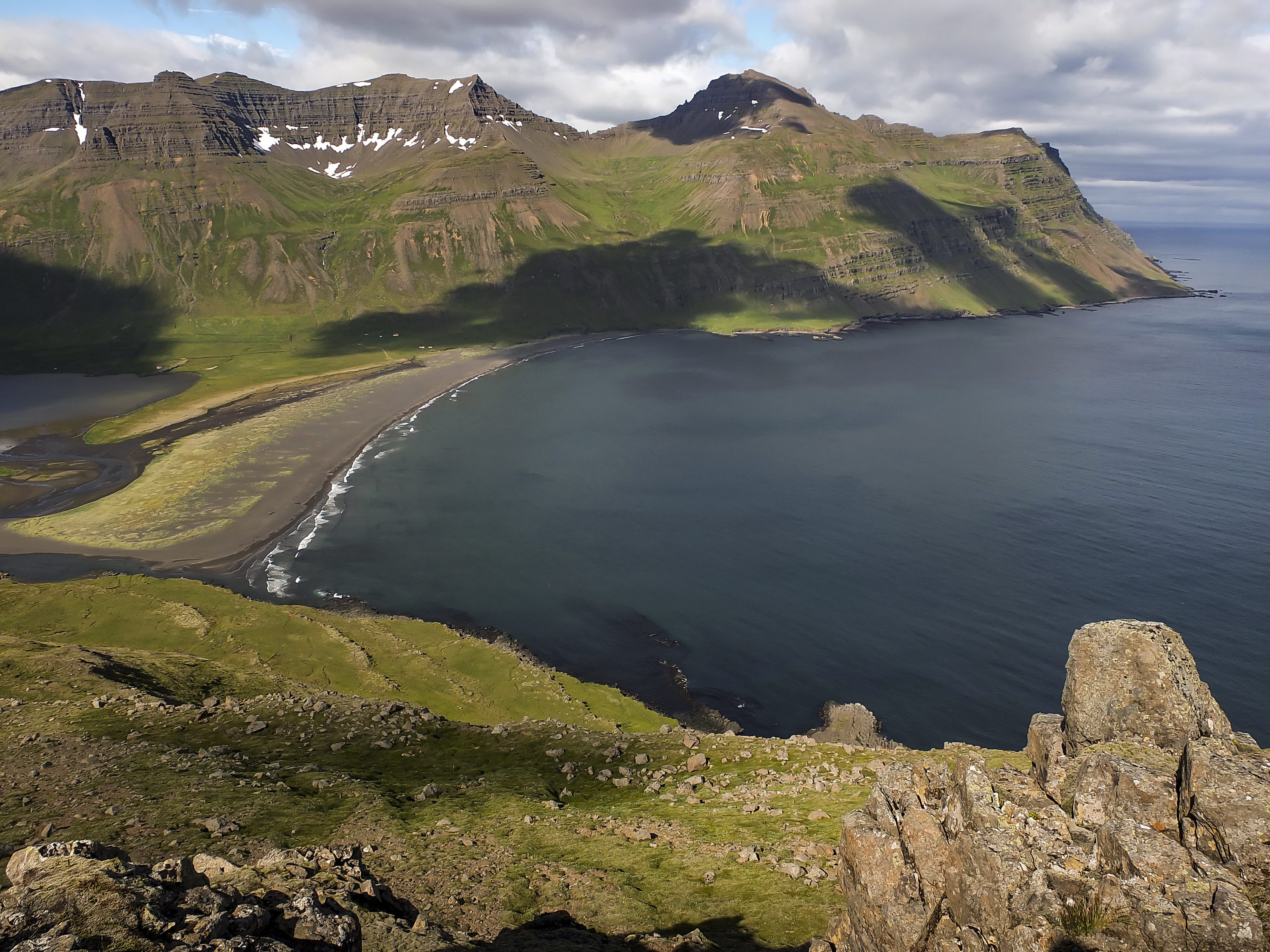 Wide view across Vöðlavík Bay, its black-sand shore, and the steep Eastfjords slopes around the cove.